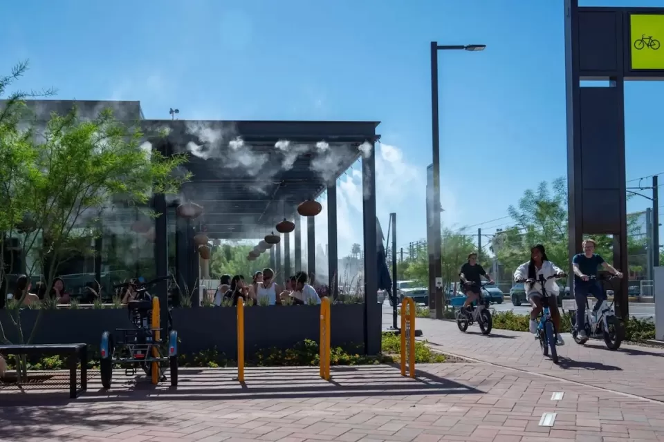 People ride bikes past outdoor restaurant patio with misters in Culdesac car-free development, Tempe, Arizona.